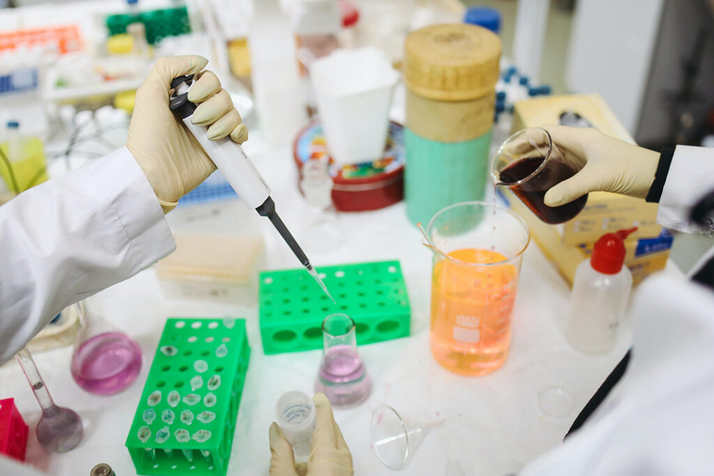 Scientific tools being handled by gloved hands on a lab table.